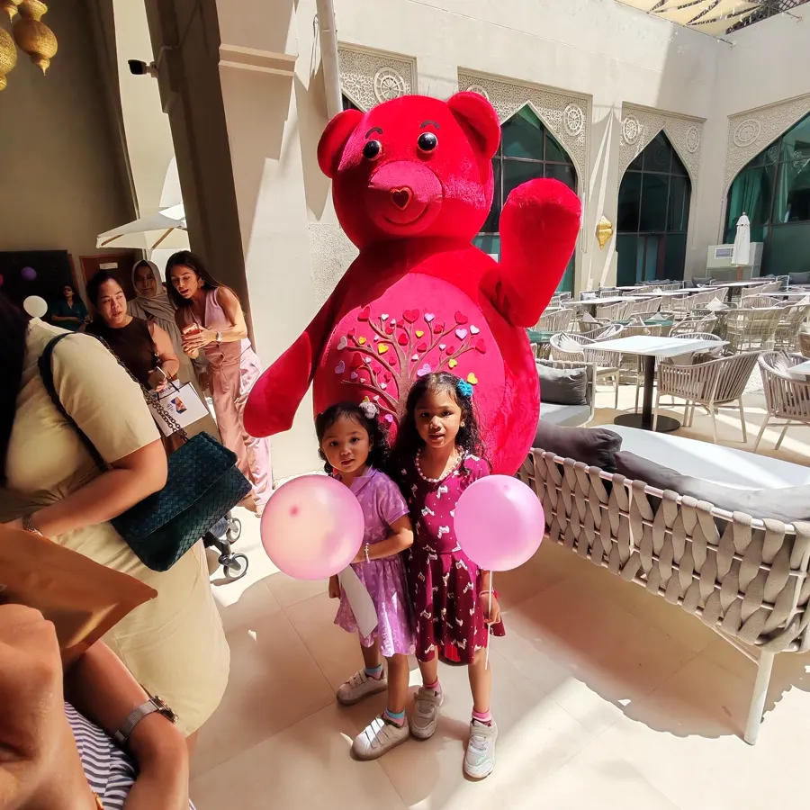 Two girls with balloons and the red YogaBears mascot at an outdoor party